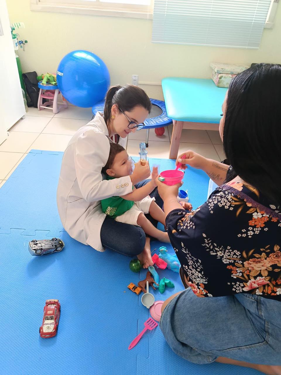 Fisioterapeuta realizando fisioterapia respiratória em criança, com a mãe ao lado